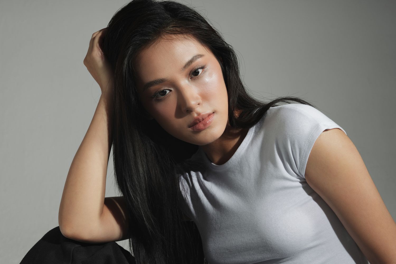 Model with long hair sitting against gray backdrop.